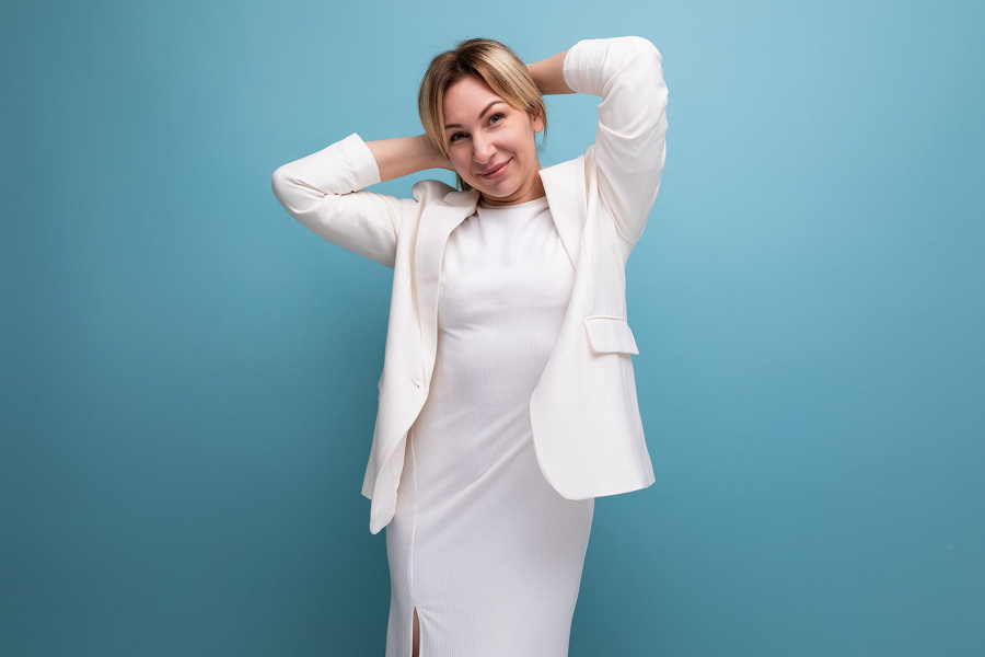 A woman wears a white tailored blazer over a white dress for a party.